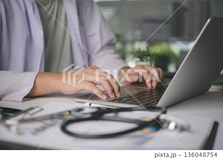 Male physician using computer for online patient consultation, managing digital health records, medical diagnosis on desk with stethoscope, representing telehealth and modern healthcare services. Male physician using computer for online patient consultation, managing digital health records, medical diagnosis on desk with stethoscope, representing telehealth and modern healthcare services. 136048754