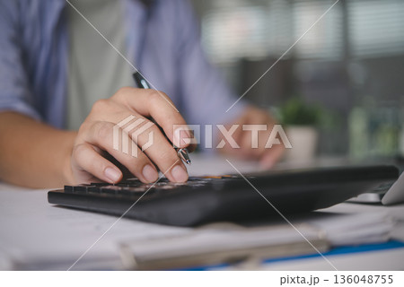 Accountant calculating finance data on calculator, working on business documents, audit report, money management, tax season, investment analysis, financial planning with paperwork at the office. 136048755