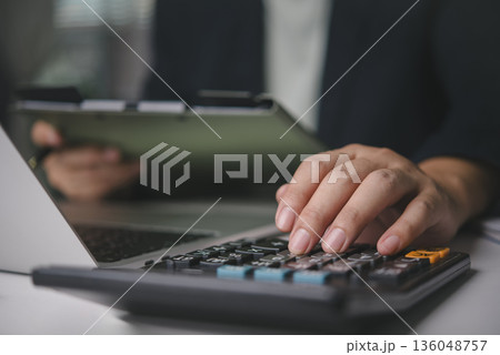 Accountant hand using calculator business finance, calculating tax, budget planning, financial analysis of documents on clipboard, working at office desk with laptop, bookkeeping and audit concept. 136048757