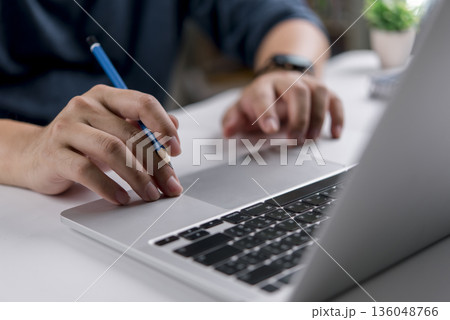 Designer or student hand holding pencil working on laptop at desk. Concept for creative process, project planning, online learning, e-learning, brainstorming ideas, or working from home office. Designer or student hand holding pencil working on laptop at desk. Concept for creative process, project planning, online learning, e-learning, brainstorming ideas, or working from home office. 136048766