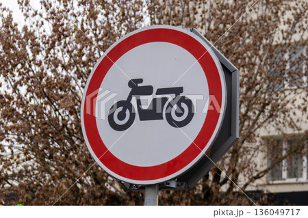 A sign prohibiting motorcycles captures attention amidst a serene scene of leafless trees and muted urban colors, hinting at winter's chill A sign prohibiting motorcycles captures attention amidst a serene scene of leafless trees and muted urban colors, hinting at winter's chill 136049717