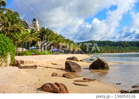 Iceland Phu Quoc Vietnam 5.7.2025. A beach with a large rock in the water and a small building in the background 136050116