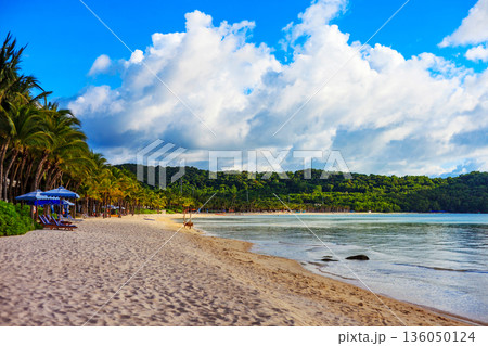 A beach with a blue umbrella and a few chairs 136050124