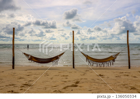 Two beach hammocks are hanging from two wooden posts on a beach Two beach hammocks are hanging from two wooden posts on a beach 136050334