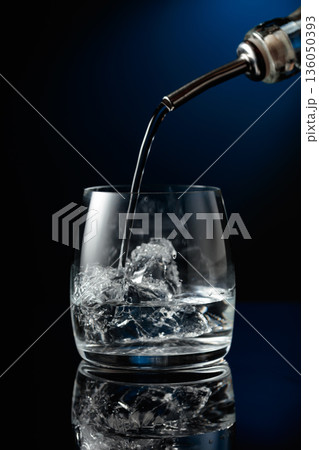 Crystal clear vodka being poured over ice in a glass. Crystal clear vodka being poured over ice in a glass. 136050393