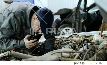 Professional automotive technician documenting engine repair, photographing vehicle components using smartphone while standing in workshop Professional automotive technician documenting engine repair, photographing vehicle components using smartphone while standing in workshop 136051020