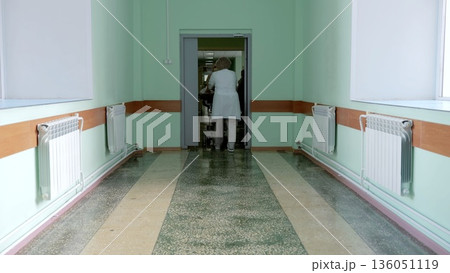 Russia Tomsk 05.07.2025: Nurse pushing stretcher down corridor, mint green walls, radiators, worn tile floor, fluorescent lighting, clinical teamwork during patient transfer, focused Russia Tomsk 05.07.2025: Nurse pushing stretcher down corridor, mint green walls, radiators, worn tile floor, fluorescent lighting, clinical teamwork during patient transfer, focused 136051119