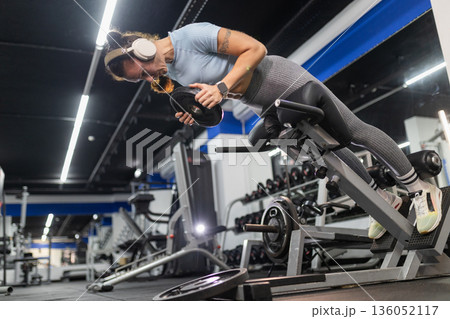 Woman exercising back muscles on hyperextension machine Woman exercising back muscles on hyperextension machine 136052117