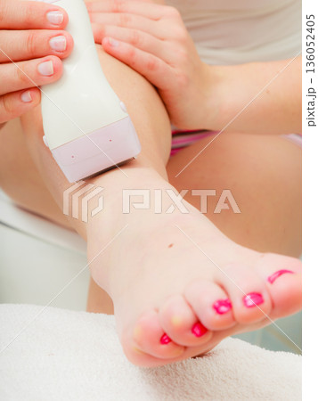 Woman shaving legs with depilator in bathroom Woman shaving legs with depilator in bathroom 136052405