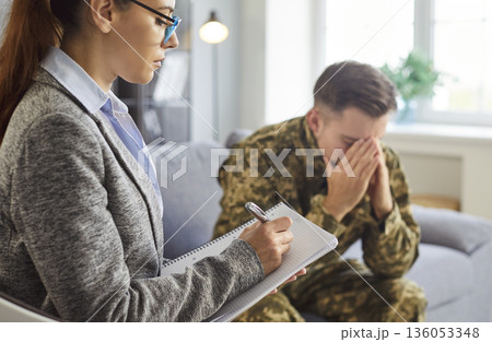 Mental health professional making notes while listens psychological concerns of young soldier man Mental health professional making notes while listens psychological concerns of young soldier man 136053348