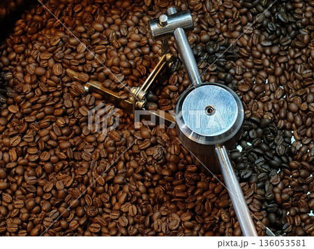 Freshly roasted coffee beans fill frame, showcasing their rich brown color and texture. roasting machine metallic component is visible, emphasizing coffee making process Freshly roasted coffee beans fill frame, showcasing their rich brown color and texture. roasting machine metallic component is visible, emphasizing coffee making process 136053581