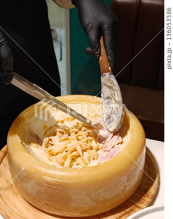 Creamy pasta being served from large cheese wheel, showcasing delicious blend of flavors. dish is prepared with care, highlighting rich texture and taste of cheese Creamy pasta being served from large cheese wheel, showcasing delicious blend of flavors. dish is prepared with care, highlighting rich texture and taste of cheese 136053586