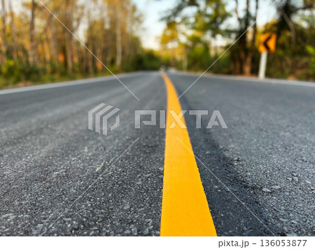 an empty asphalt road with a yellow center line leading forward, surrounded by trees and soft sunlight, symbolizing journey, direction, progress, travel, and new beginnings an empty asphalt road with a yellow center line leading forward, surrounded by trees and soft sunlight, symbolizing journey, direction, progress, travel, and new beginnings 136053877