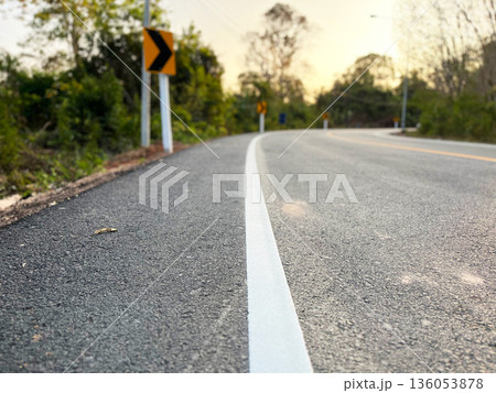a curved asphalt road with a white edge line and warning signs, surrounded by trees at sunset, symbolizing direction, decision making, caution, journey, change, and future path a curved asphalt road with a white edge line and warning signs, surrounded by trees at sunset, symbolizing direction, decision making, caution, journey, change, and future path 136053878
