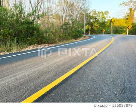 an empty asphalt road with a yellow center line leading forward, surrounded by trees and soft sunlight, symbolizing journey, direction, progress, travel, and new beginnings an empty asphalt road with a yellow center line leading forward, surrounded by trees and soft sunlight, symbolizing journey, direction, progress, travel, and new beginnings 136053879
