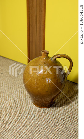 Brown ceramic jug with handle on textured carpet by yellow wall Brown ceramic jug with handle on textured carpet by yellow wall 136054318