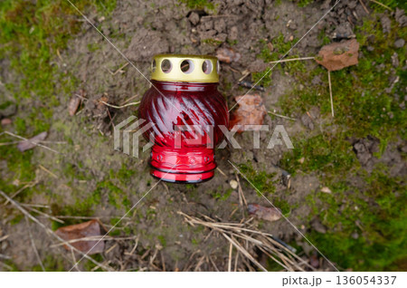Red glass remembrance candle on mossy ground with fallen leaves 136054337