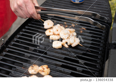Grilling shrimp skewers on bbq grill with tongs 136054338