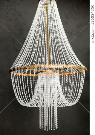 Elegant beaded chandelier with brass frame against dark backdrop 136054350