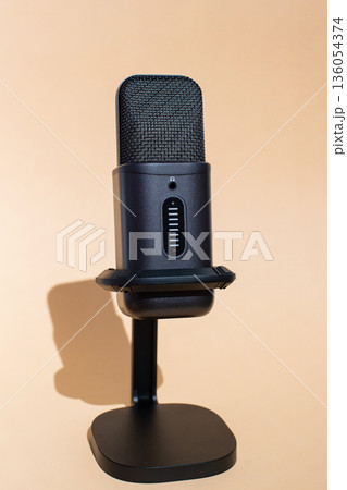 Black professional microphone on stand against beige background. International Podcast Day Black professional microphone on stand against beige background. International Podcast Day 136054374
