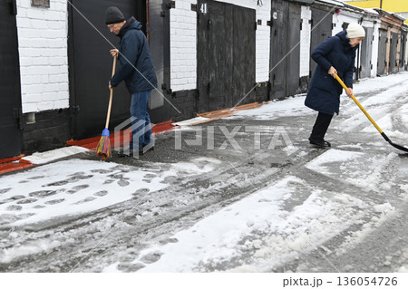 Man shovels snow from a pathway during winter in a city Man shovels snow from a pathway during winter in a city 136054726