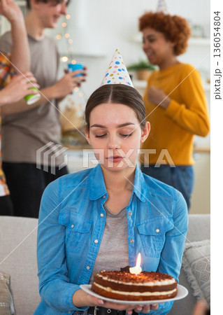 Sad lonely frustrated unhappy young woman looking at birthday cake with candle on birthday party. Girl sad disappointed thinking about life. Birthday party with friends. People celebrating birthday Sad lonely frustrated unhappy young woman looking at birthday cake with candle on birthday party. Girl sad disappointed thinking about life. Birthday party with friends. People celebrating birthday 136054804