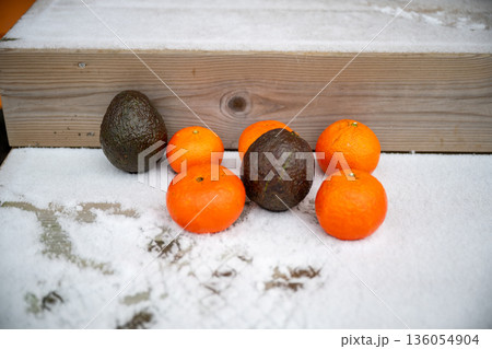 Fresh citrus fruit and avocados on snowy wooden steps in winter Fresh citrus fruit and avocados on snowy wooden steps in winter 136054904