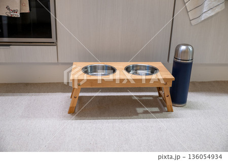 Elevated wooden pet feeding station with double bowl and thermos in modern kitchen Elevated wooden pet feeding station with double bowl and thermos in modern kitchen 136054934