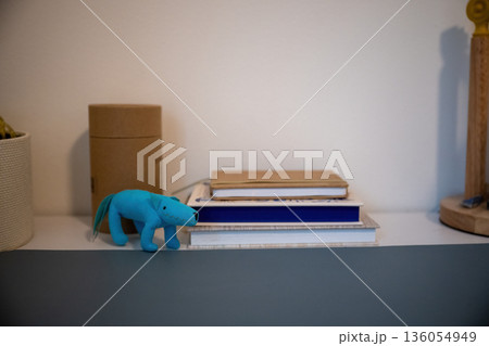 Minimal still life with blue toy dinosaur on bookshelf with notebooks and cardboard boxes in cozy home interior 136054949