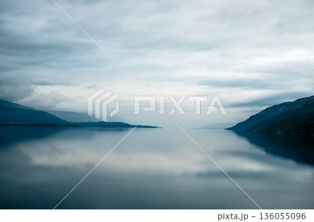 Calm fjord lake with misty mountains and dramatic cloudy sky in Norway 136055096
