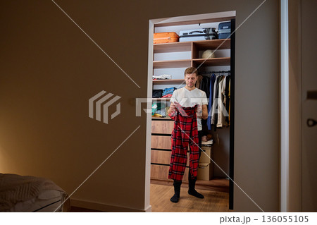 Man standing in walk in closet and holding clothes while choosing outfit 136055105