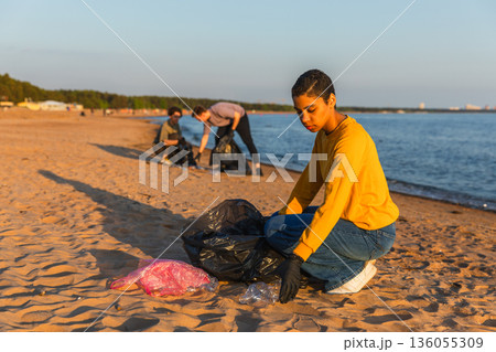 Earth day. Volunteers activists team collects garbage cleaning of beach coastal zone. Woman mans puts plastic trash in garbage bag on ocean shore. Environmental conservation coastal zone cleaning 136055309