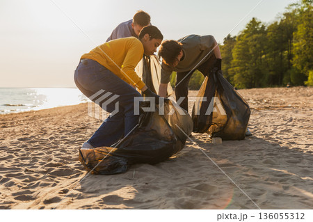 Earth day. Volunteers activists collects garbage cleaning of beach coastal zone. Woman and mans puts plastic trash in garbage bag on ocean shore. Environmental conservation coastal zone cleaning 136055312