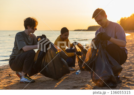 Earth day. Volunteers activists team collects garbage cleaning of beach coastal zone. Woman mans puts plastic trash in garbage bag on ocean shore. Environmental conservation coastal zone cleaning 136055315