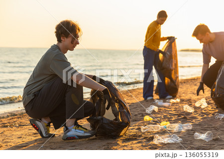 Earth day. Volunteers activists team collects garbage cleaning of beach coastal zone. Woman mans puts plastic trash in garbage bag on ocean shore. Environmental conservation coastal zone cleaning Earth day. Volunteers activists team collects garbage cleaning of beach coastal zone. Woman mans puts plastic trash in garbage bag on ocean shore. Environmental conservation coastal zone cleaning 136055319