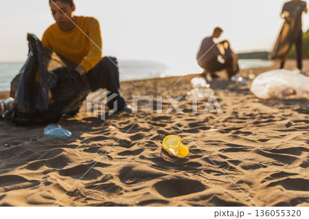 Earth day. Volunteers activists collects garbage cleaning of beach coastal zone. Woman mans with trash in garbage bag on ocean shore. Environmental conservation coastal zone cleaning. Blurred image Earth day. Volunteers activists collects garbage cleaning of beach coastal zone. Woman mans with trash in garbage bag on ocean shore. Environmental conservation coastal zone cleaning. Blurred image 136055320
