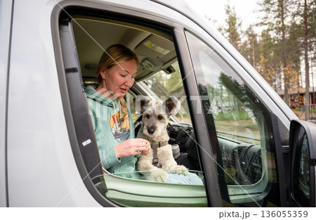 Woman traveling in camper van with dog looking through window enjoying road trip lifestyle Woman traveling in camper van with dog looking through window enjoying road trip lifestyle 136055359
