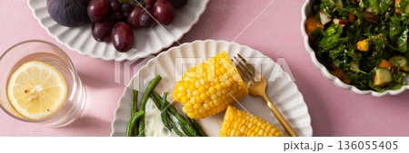 A healthy breakfast is served on a pink table. There are plates with asparagus, a fried egg, corn, and a fresh salad. Grapes and sunflower seeds are on the side, banner A healthy breakfast is served on a pink table. There are plates with asparagus, a fried egg, corn, and a fresh salad. Grapes and sunflower seeds are on the side, banner 136055405