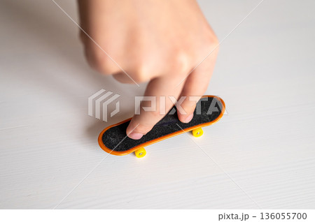 children's hands playing with toy fingerboard with yellow wheels on white background, selective focus 136055700