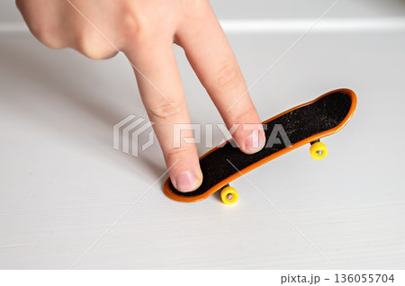 children's hands playing with toy fingerboard with yellow wheels on white background, selective focus children's hands playing with toy fingerboard with yellow wheels on white background, selective focus 136055704