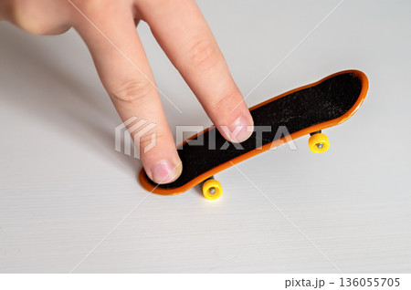 children's hands playing with toy fingerboard with yellow wheels on white background, selective focus children's hands playing with toy fingerboard with yellow wheels on white background, selective focus 136055705