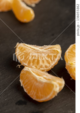sliced juicy peeled orange tangerine on a black slate table, ripe orange small mandarin without peel on a slate board, tangerine divided into small slices 136055862