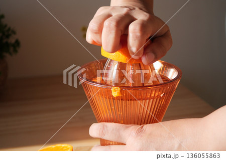 Squeezing orange juice using a manual juicer in the kitchen 136055863