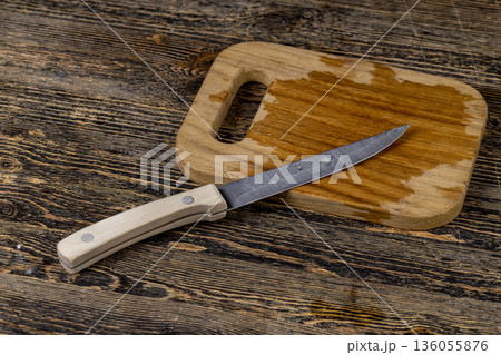 An empty wooden cutting board is wet after food and a sharp knife, a sharp steel knife is lying on a wooden cutting board wet from water An empty wooden cutting board is wet after food and a sharp knife, a sharp steel knife is lying on a wooden cutting board wet from water 136055876