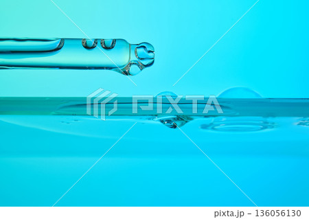 Dropper dispensing clear serum liquid against blue background Dropper dispensing clear serum liquid against blue background 136056130