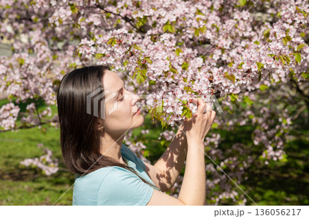 Portrait of a young woman admiring blooming sakura in a sunny spring park Portrait of a young woman admiring blooming sakura in a sunny spring park 136056217