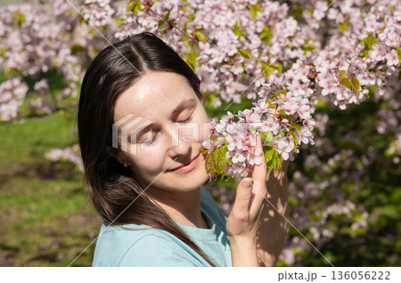 Young woman with closed eyes enjoying scent of cherry blossoms in peaceful spring park 136056222