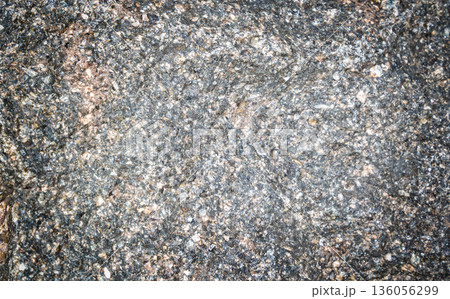 Close-up view of textured granite rock surface displaying various mineral deposits and color variations, showcasing natural geological features and patterns Close-up view of textured granite rock surface displaying various mineral deposits and color variations, showcasing natural geological features and patterns 136056299