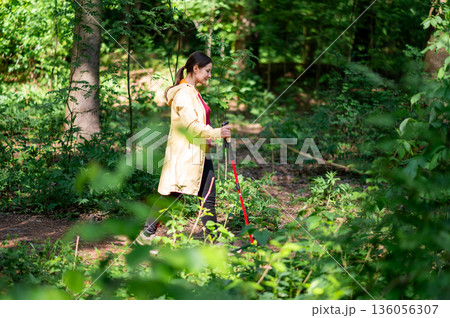 Active middle-aged woman walking with Nordic poles in summer forest, promoting healthy living and physical well-being Active middle-aged woman walking with Nordic poles in summer forest, promoting healthy living and physical well-being 136056307