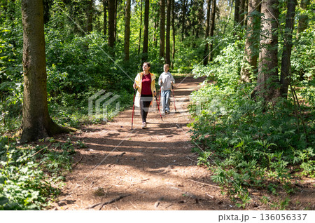 Mother and son walking through a sunny forest, practicing Nordic walking outdoors Mother and son walking through a sunny forest, practicing Nordic walking outdoors 136056337